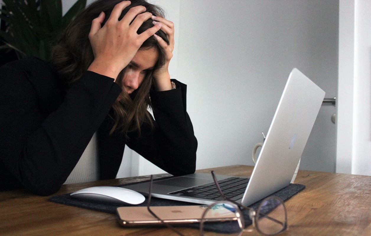 A woman in a black blazer with her hands to her head frustrated at her laptop screen