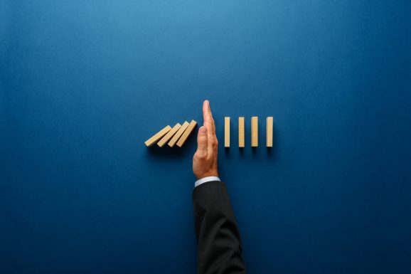 Top view of businessman hand stopping falling dominos in a business crisis management conceptual image.