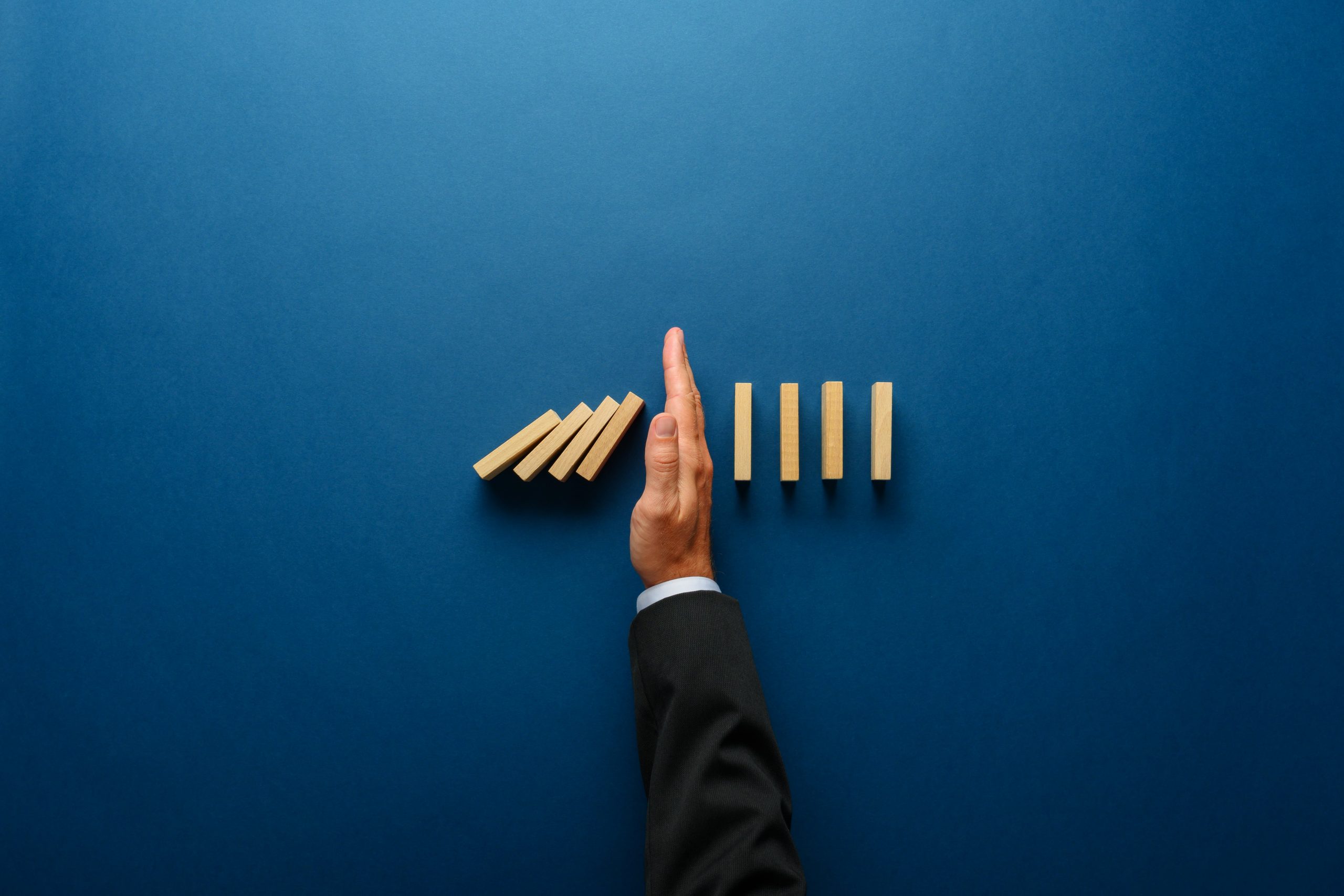 Top view of businessman hand stopping falling dominos in a business crisis management conceptual image.