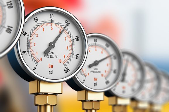 A picture of an oil and gas fuel manufacturing industry concept. A row of metal steel high pressure gauge meters or manometers on tubing pipeline.