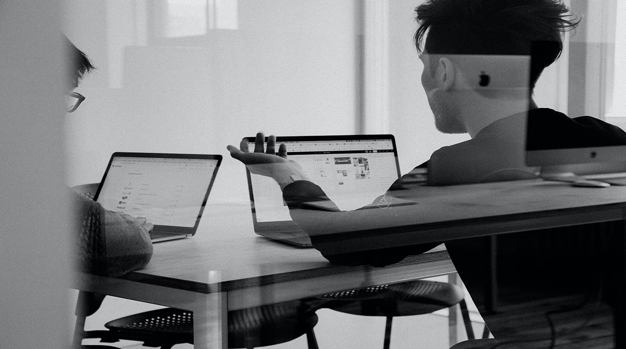 black and white image of investors engaging in a conversation in front of their laptops